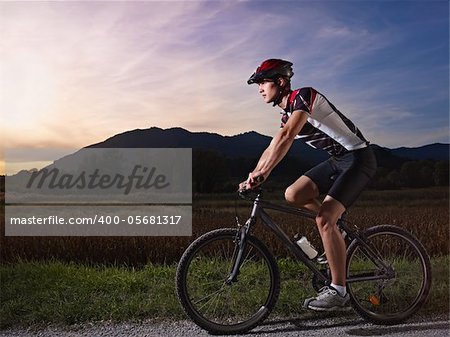 sports activity: young adult cyclist riding fast mountain bike in the countryside. Horizontal shape, side view, full length, copy space