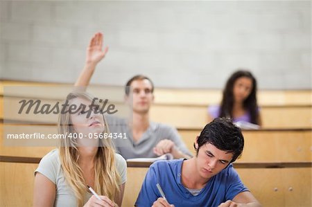 Student raising his hand while his classmates are taking notes in an amphithater