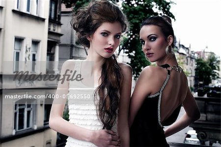 fashion shot of two attractive and elegant girl friend outside in a balcony with old fashion style building in background