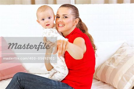 Happy mother sitting on divan and showing something to her baby