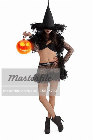 very pretty young brunette in black witch dress with hat and high heel ready for halloween standing with party ball against white background