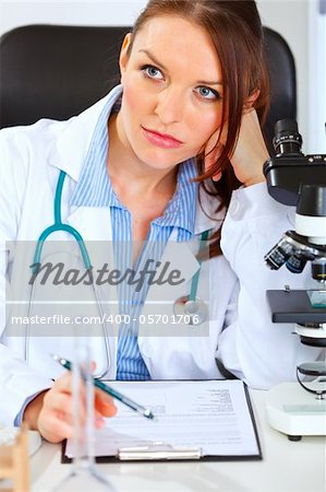 Thoughtful doctor woman sitting at office table