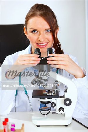 Smiling female medical doctor using microscope