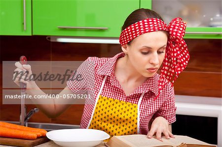 Serious woman in the kitchen with knofe is reading recipe book