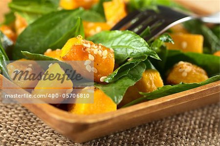 Baked pumpkin, spinach and sesame salad (Selective Focus, Focus on the pumpkin piece with many sesame seeds in the front)