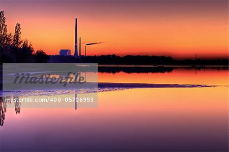 Scenic view of power plant near beach in calm water at sunset