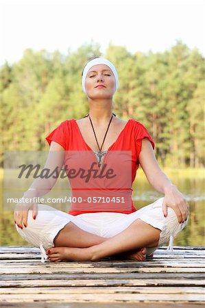 A picture of a pretty young woman practicing yoga over natural green background by the lake