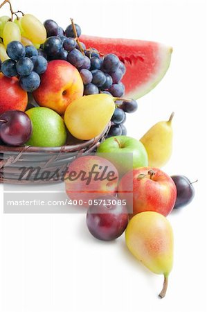 Various fresh ripe fruits placed in a wicker basket and around on white background.