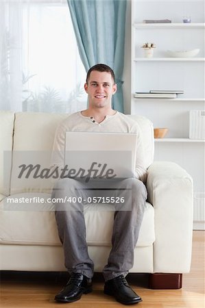 Portrait of a man using a laptop while sitting on a sofa in his living room