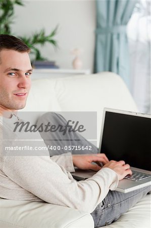 Portrait of a man lying on his couch with a laptop looking at the camera