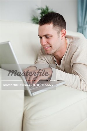 Portrait of a smiling man lying on a couch using a laptop in his living room