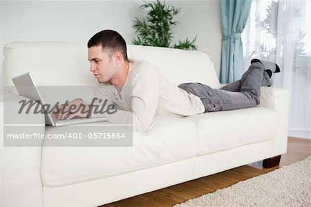 Handsome man lying on a couch using a laptop in his living room