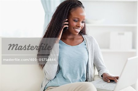 Smiling woman on sofa with smartphone and laptop