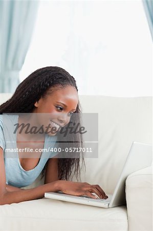 Close up of smiling woman lying on the sofa working with her notebook