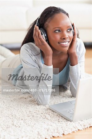 Close up of smiling woman lying on the floor with her notebook listening to music