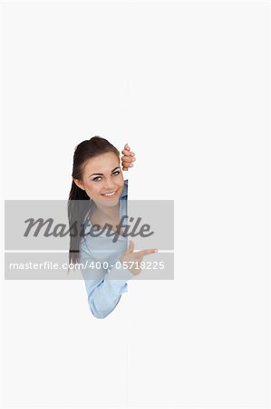 Smiling businesswoman looking around the corner while pointing against a white background