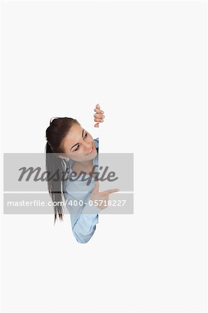 Businesswoman pointing while looking around the corner against a white background