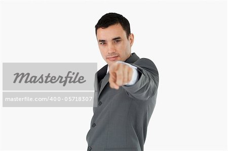 Side view of young businessman pointing towards camera against a white background
