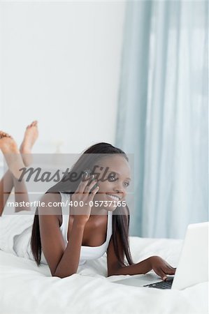 Portrait of a happy woman using a laptop while making a phone call in her bedroom