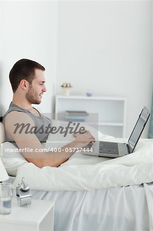 Portrait of a happy man using a laptop in his bedroom