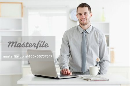 Businessman using a laptop while drinking tea in his kitchen