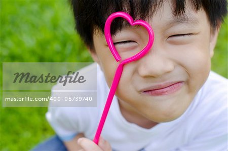 Cute Asian boy holding a heart shape on his eye