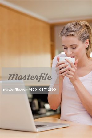 Portrait of a young woman using a laptop while drinking tea in her kitchen