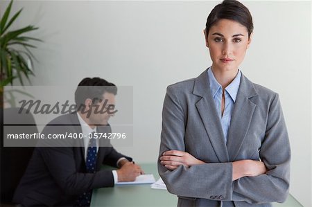 Professional businesswoman posing while her colleague is working in an office
