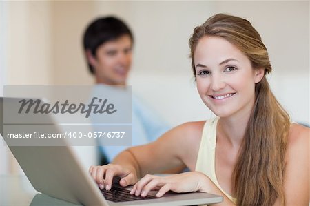 Woman using a laptop while her husband is sitting on a couch in their living room