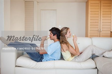 Couple sitting back to back while drinking wine in their living room
