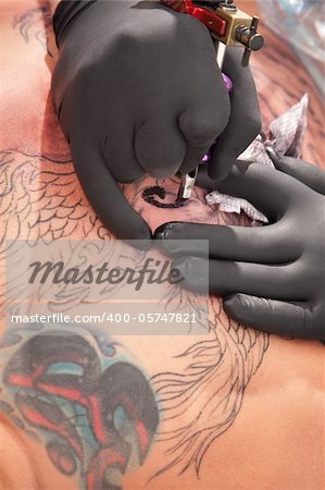 Tatto artist with black gloves inks the outline of his design