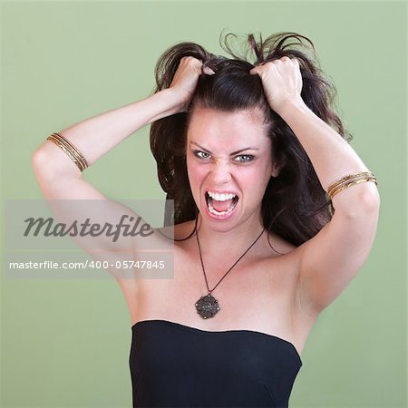 Young frustrated woman pulls her hair over green background