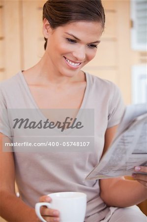 Smiling young woman reading newspaper while having coffee