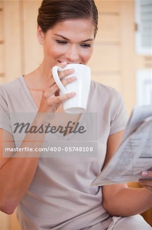 Young woman taking a sip of coffee while reading newspaper