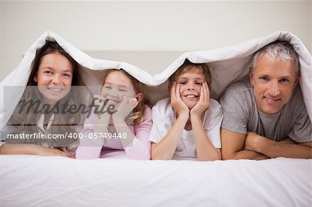 Playful family lying under a duvet in a bedroom