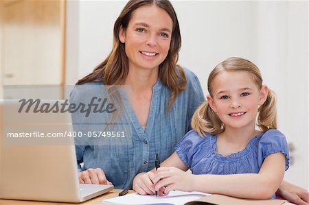 Beautiful woman helping her daughter doing her homework in a kitchen