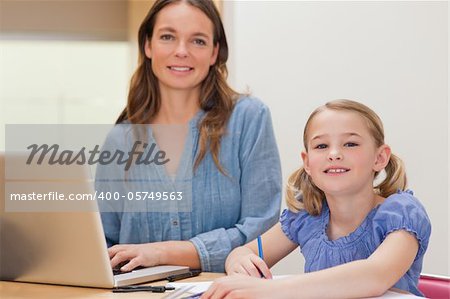 Girl doing her homework while her mother is using notebook in a kitchen