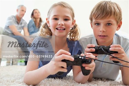 Playful siblings playing video games with their parents on the background in a living room