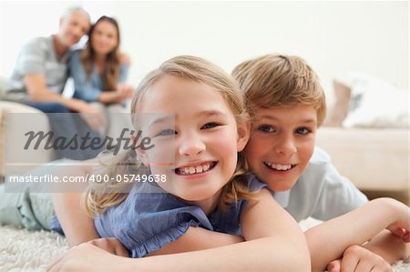 Happy siblings posing on a carpet with their parents on the background in a living room