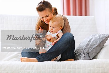 Young mom showing her interested baby photos on camera