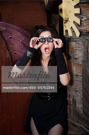 Surprised pretty fairy looks through loupe glasses in rustic location