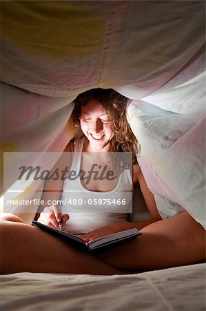 woman is sitting under cover in bed and writing her diary