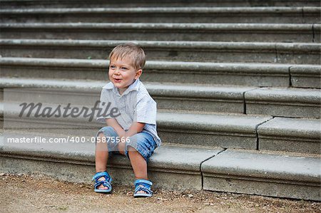 Cute little boy sits on on the stairs in a park