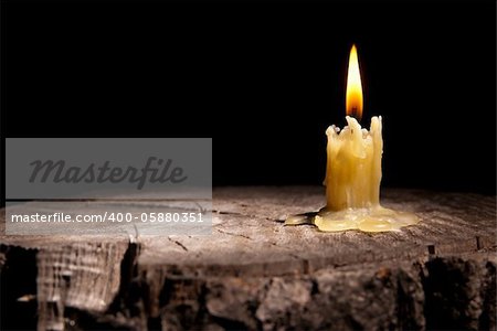 old candle stands on the stump of a tree on the black background