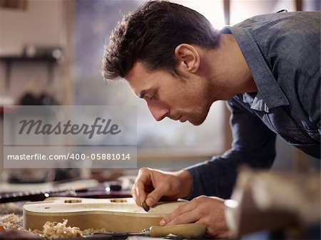 mid adult man at work as craftsman in italian workshop with guitars and musical instruments, smoothing guitar body