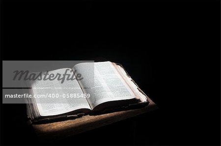 Old open bible lying on a wooden table in a beam of sunlight (not an isolated image) Shallow Depth of field â?? Focus on middle text