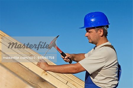 Carpenter working on the roof wooden structure - driving in big nail