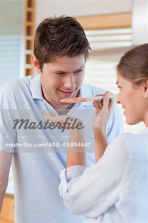 Portrait of a handsome man tasting his wife's sauce in their kitchen