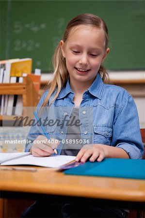 Portrait of a happy schoolgirl writing in a classroom