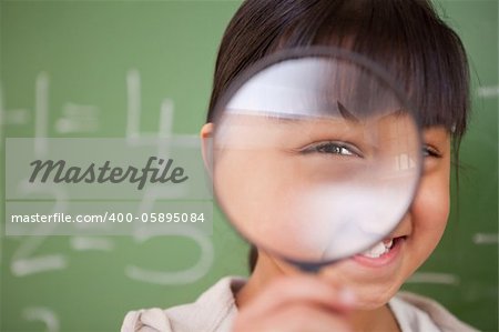 Close up of a cute schoolgirl looking through a magnifying glass in a classroom
